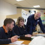 Elodie, apprentie chargée de prévention sécurité en formation en alternance à la centrale de Porcheville, échange avec son tuteur (debout) et un collègue en salle de commande